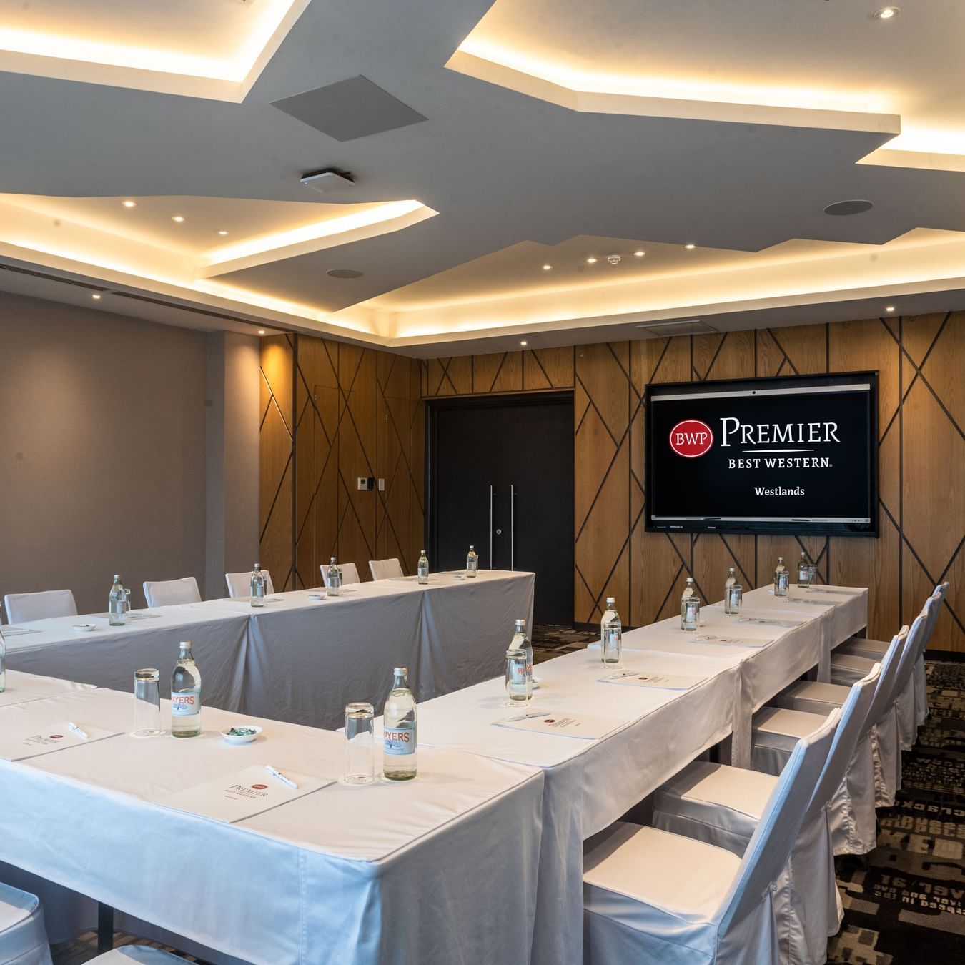 Boardroom at Best Western Premier Westlands hotel, featuring rectangular tables with white cloths, executive chairs, and a large wall-mounted display.