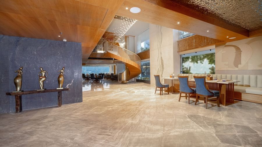 Image of a dining space with tables and chairs and a spiral staircase behind at Auradoon, Dehradun.