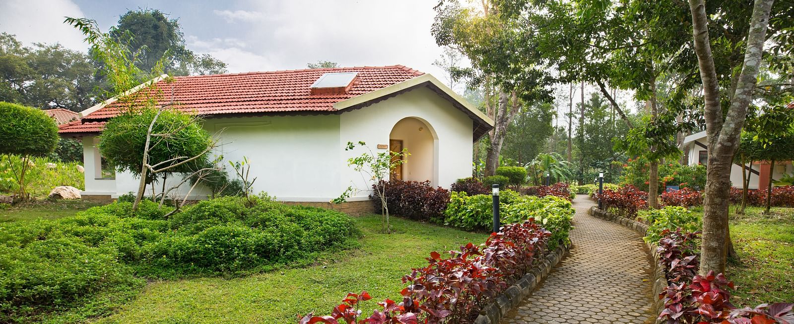 a pathway adorned with rose bushes leading to a cottage - Kadkani River Resort, Coorg