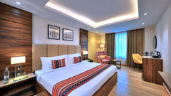 An image of a bedroom with a king size bed in the Deluxe Room with furniture to sit and relax on the side - Golden Tulip, Agra