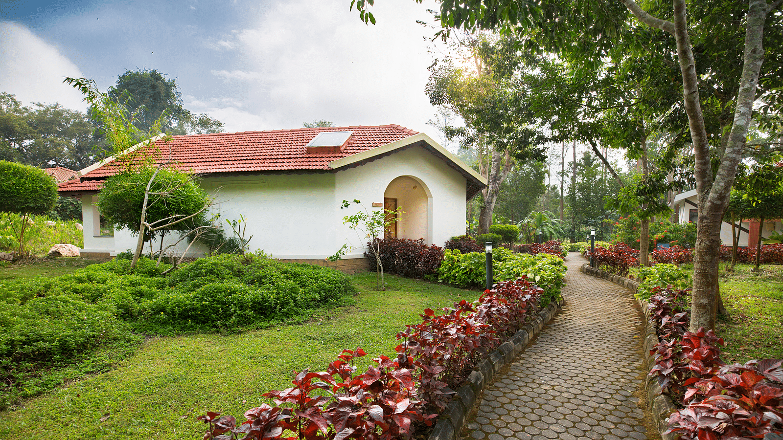 a pathway adorned with rose bushes leading to a cottage - Kadkani River Resort, Coorg