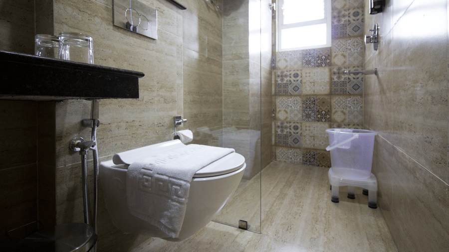 A wall-mounted toilet, a glass shower partition, and tiled walls at Valmere Lungta Boutique Hotel & Spa, Darjeeling.