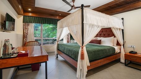 Premium Room with Balcony featuring a large bed with curtains neatly tied to rods on all four sides and a wall-mounted television