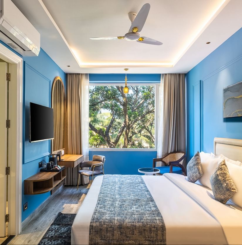 A side view of the bed with bedding in a blue colored room | Renest Calangute, Goa