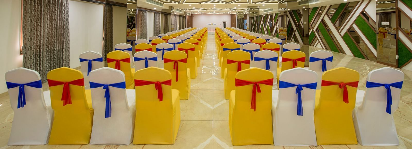 A conference room with rows of yellow chair covers and red and blue sashes, geometric ceiling designs, and a reflective modern interior at Lords Eco Inn Morbi.