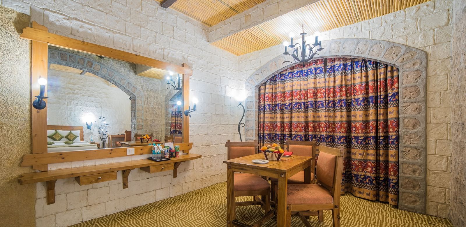 A rustic vanity area with a large mirror and traditional wooden furniture against a patterned curtain at  Sitara Luxury Hotel in Hyderabad near Ramoji Film City.