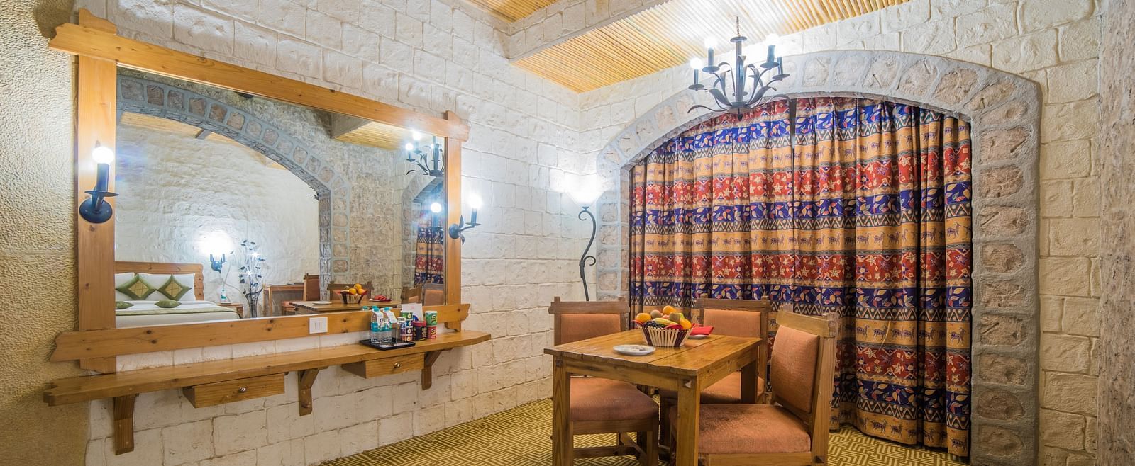 A rustic vanity area with a large mirror and traditional wooden furniture against a patterned curtain at  Sitara Luxury Hotel in Hyderabad near Ramoji Film City.