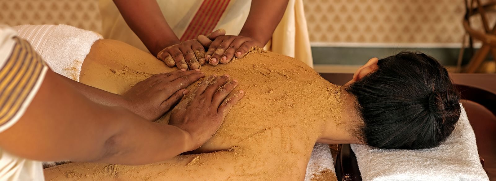 A close-up of a person receiving a massage on their back, with brown substance applied - Shreyas Retreat