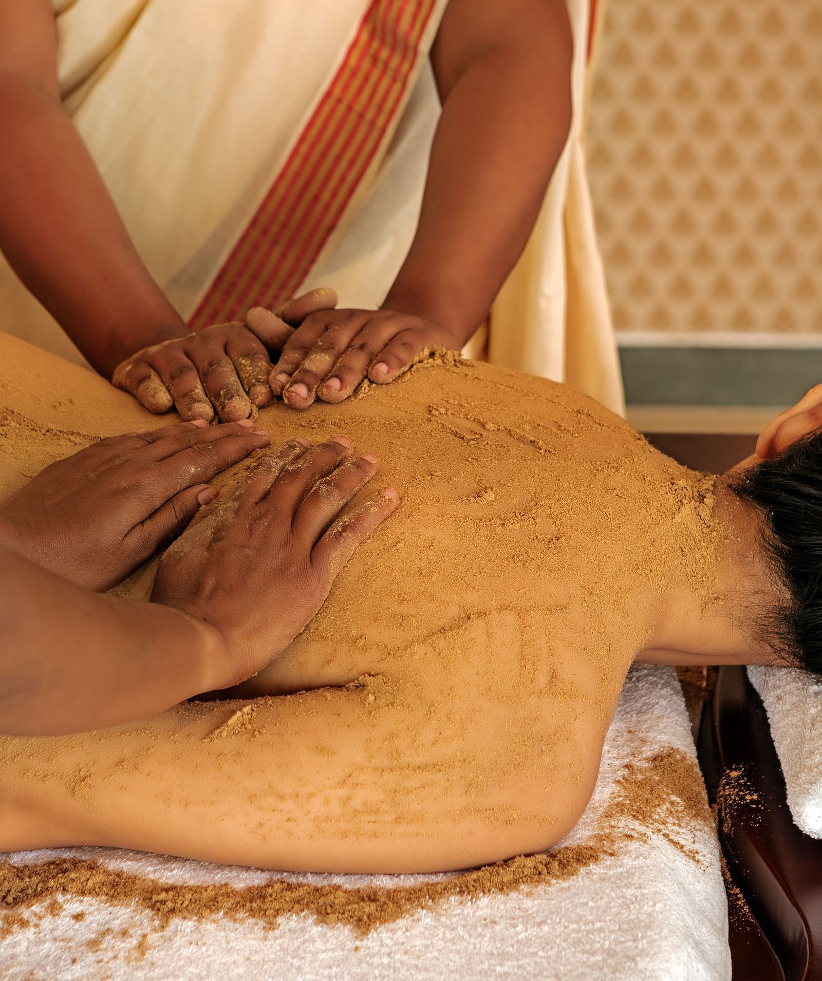 A close-up of a person receiving a massage on their back, with brown substance applied - Shreyas Retreat