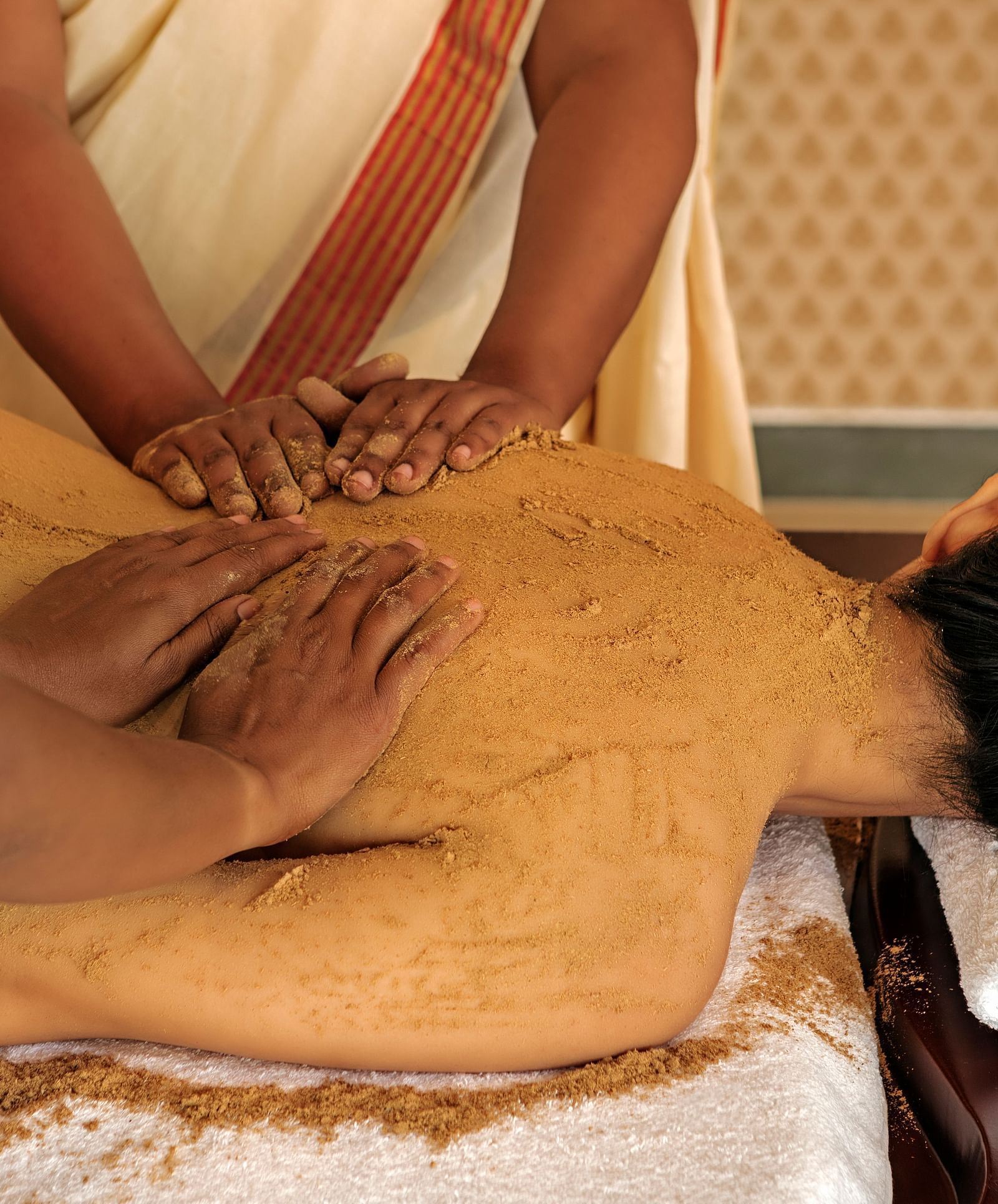 A close-up of a person receiving a massage on their back, with brown substance applied - Shreyas Retreat