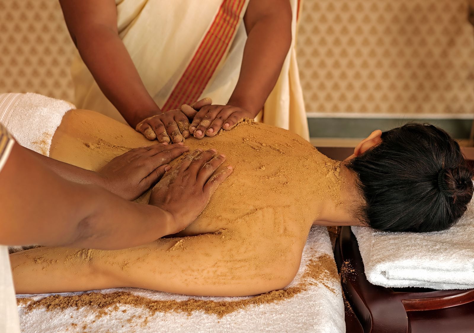 A close-up of a person receiving a massage on their back, with brown substance applied - Shreyas Retreat