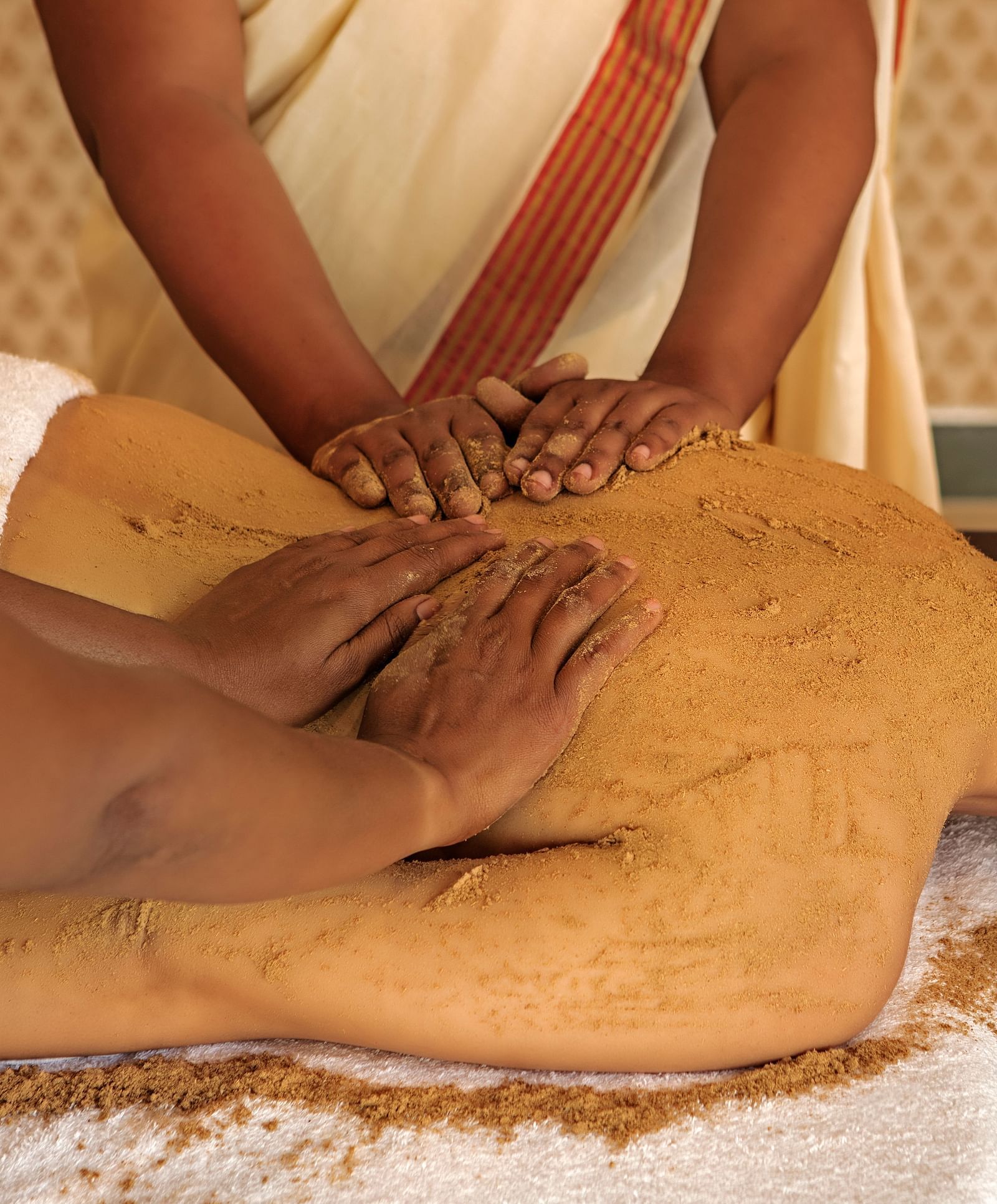 A close-up of a person receiving a massage on their back, with brown substance applied - Shreyas Retreat