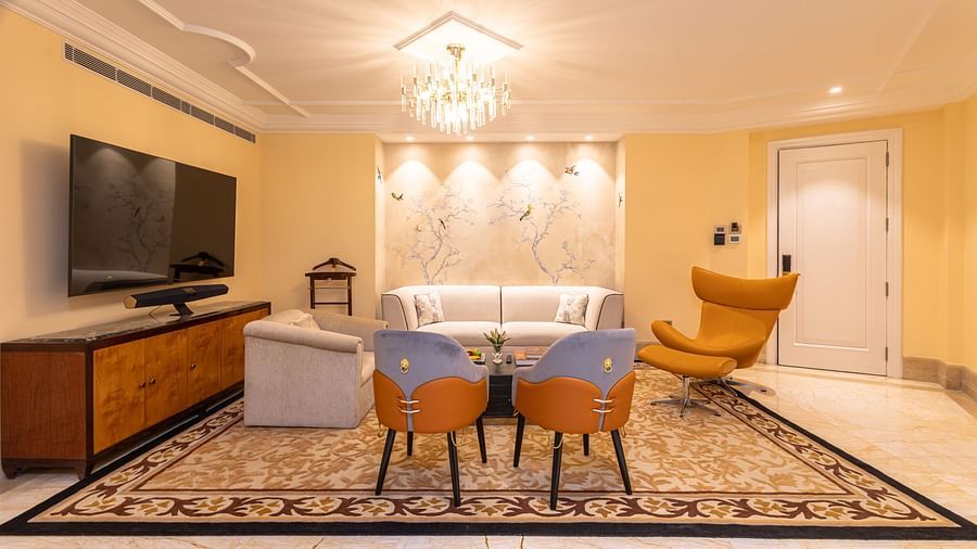 image of a brightly lit living area with two cushioned chairs and white leather couch and wall mounted tv at our lutyens luxury suite - The Claridges New Delhi