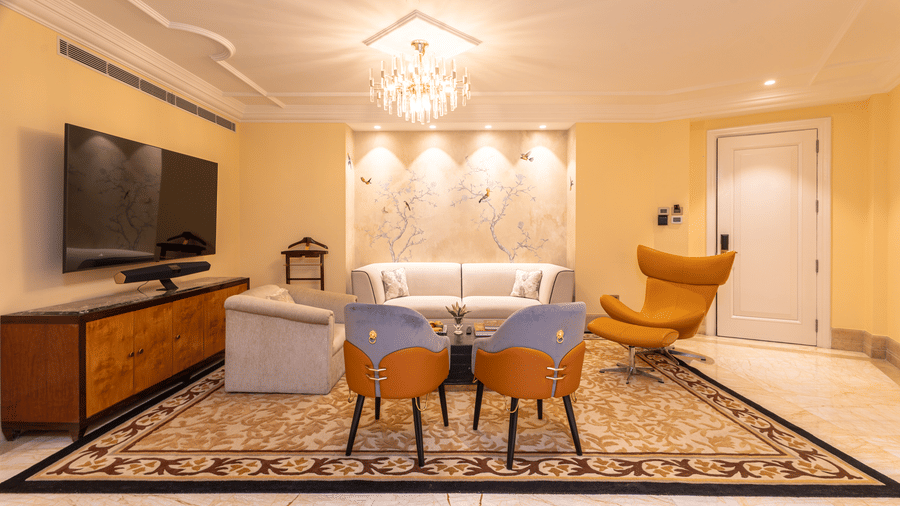 image of a brightly lit living area with two cushioned chairs and white leather couch and wall mounted tv at our lutyens luxury suite - The Claridges New Delhi