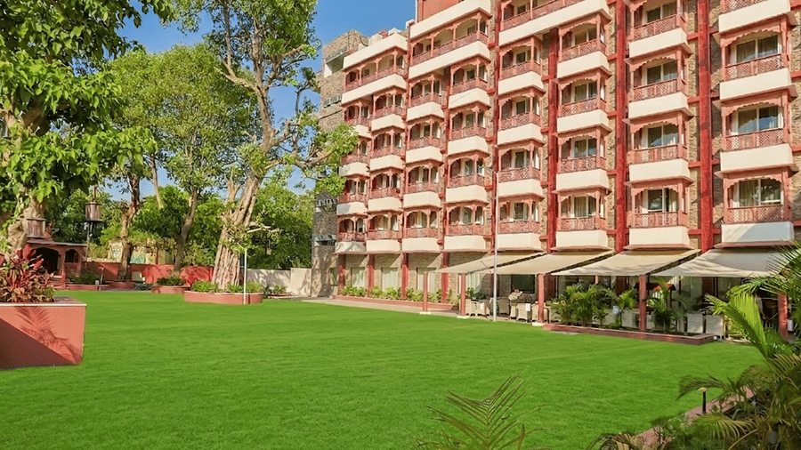 Multi-story hotel building with balconies overlooking a manicured green lawn and covered outdoor seating area at Bhagirathi by Atishay.