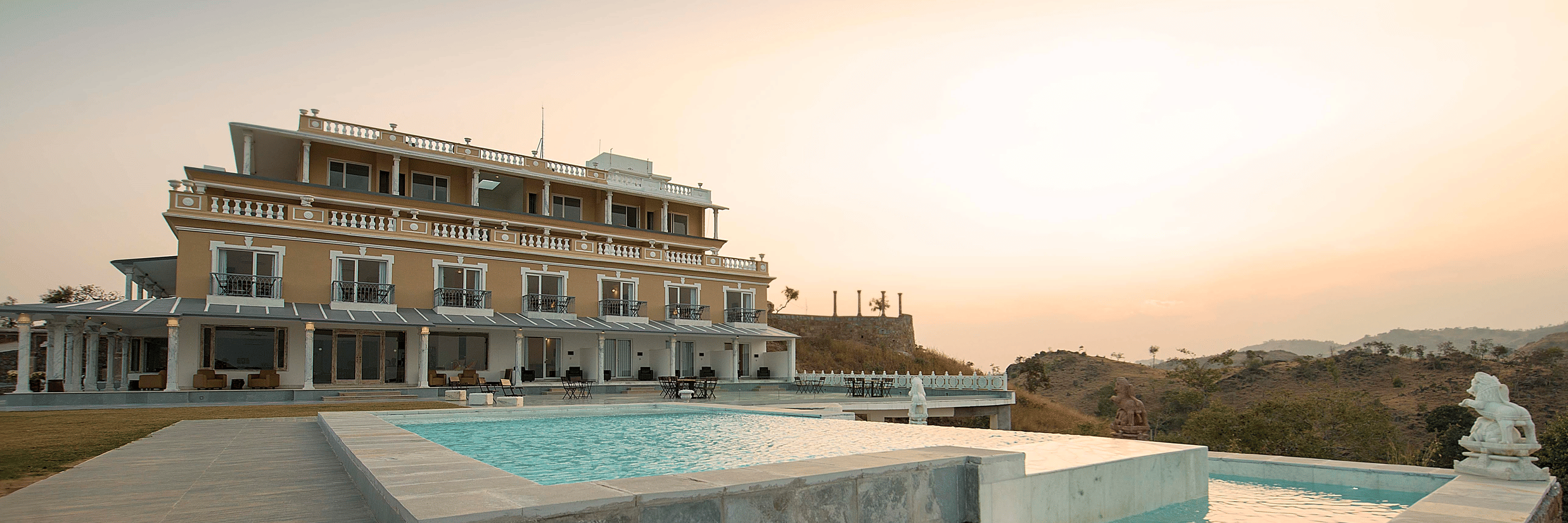 Facade of Fateh Safari Resort, Kumbhalgarh with a pool in front of it during sunset 