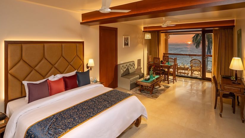  Lounge Seaview Suite at Uday Samudra Leisure Beach Hotel featuring a plush king size bed with colourful pillows, a seating area, and a balcony overlooking the sea at sunset