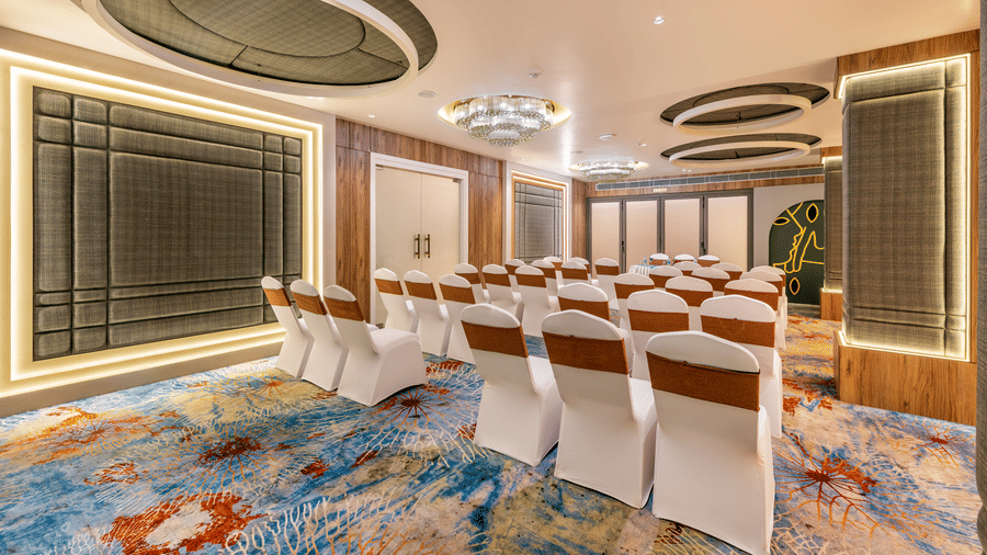 Elegant banquet hall at Lords Inn Sangam, Bhopal arranged with white and gold chairs, round ceiling light fixtures, and decorative wall paneling.