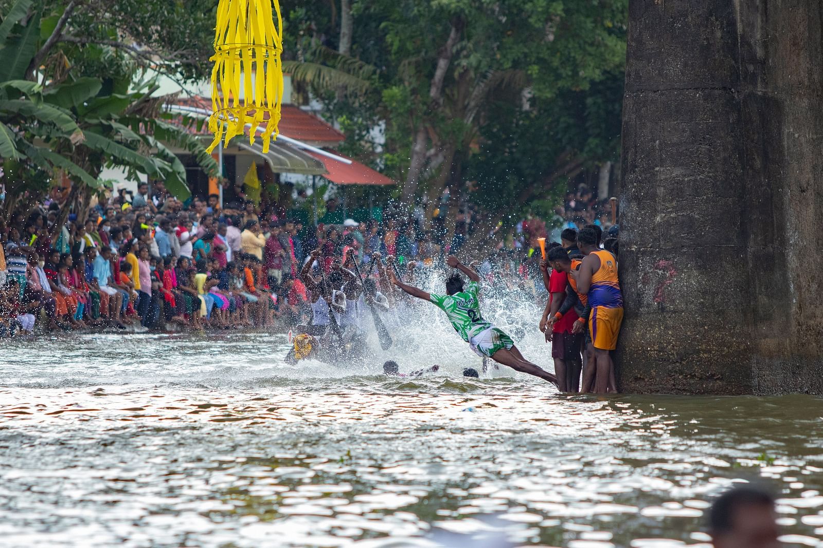 A group of people standing on the edge of the waterbody while a boat is passing by during a race.