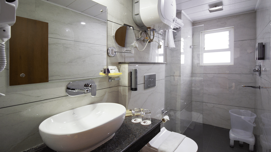 A wash basin on a counter, a toilet, a glass shower partition, and a water heater in a hotel bathroom at Valmere Lungta Boutique Hotel & Spa, Darjeeling.