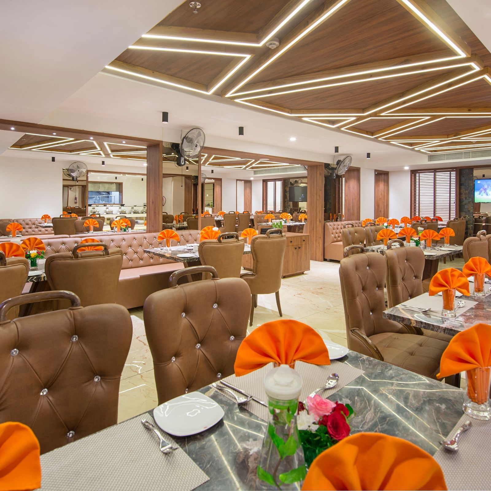 A lively restaurant dining area with multiple tables set for service, featuring warm lighting and decorative ceiling panels at Lords Eco Inn Morbi.