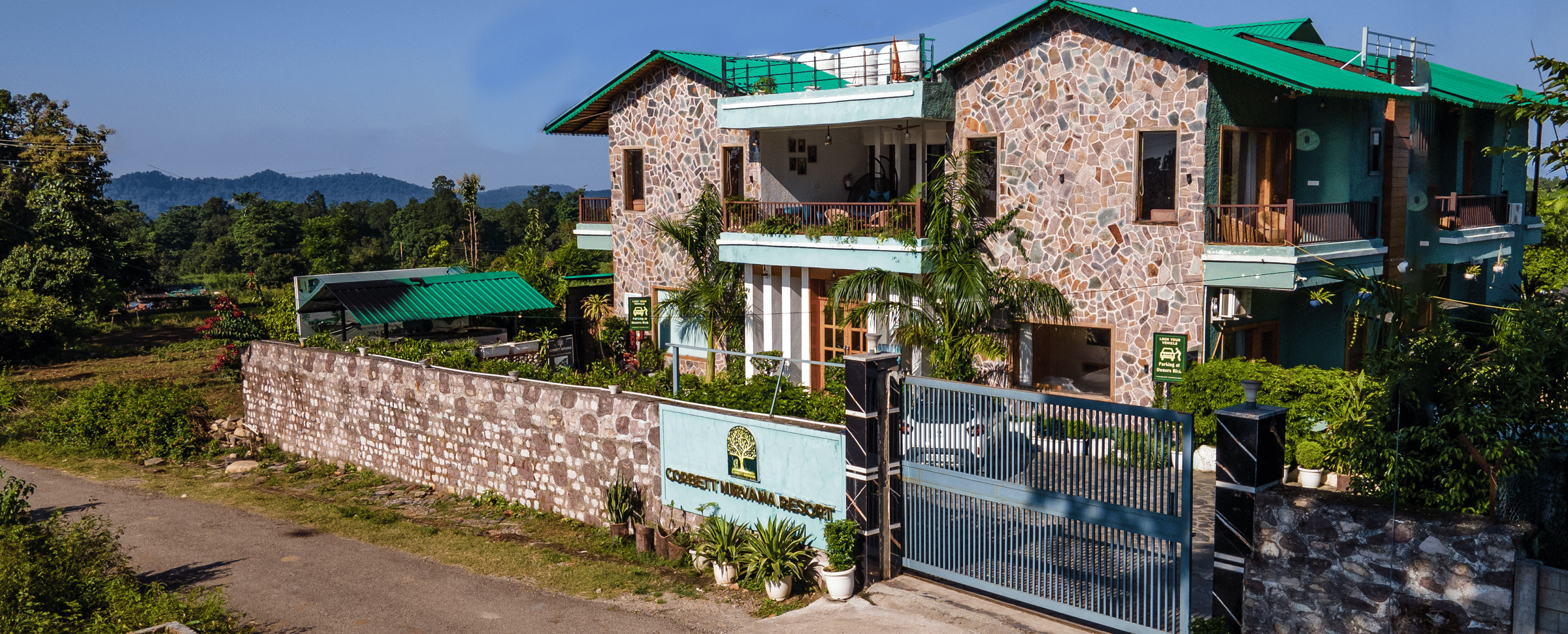 Day-time exterior view of the stone-clad main building of Corbett Nirvana Resort with green roof accents