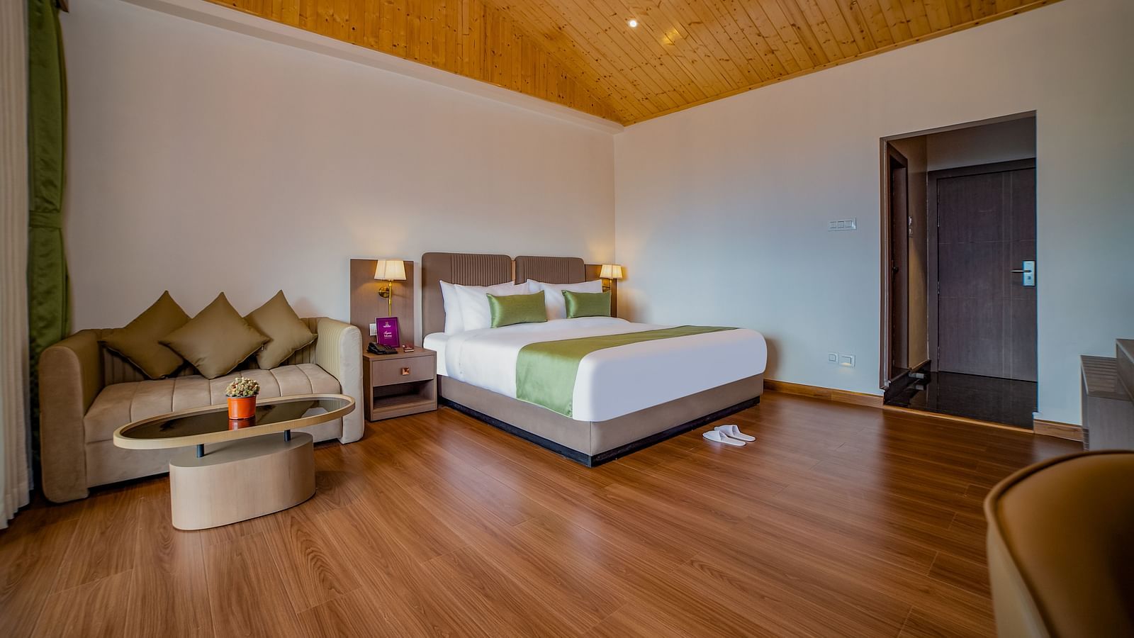 Modern hotel room with a large bed, wooden flooring, a cosy seating area with a sofa and coffee table, and a wooden vaulted ceiling - Yashshree Pelling Chekhim Retreat.