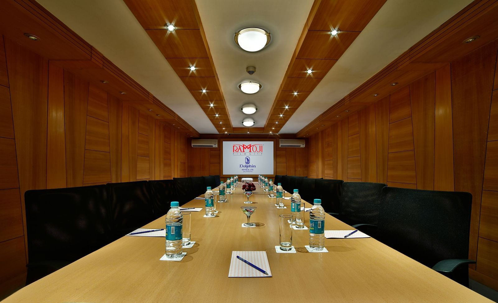 A sleek boardroom with a wooden table, leather chairs, and a screen for presentations. - Tara, Comfort Hotel in Hyderabad - Ramoji Film City.