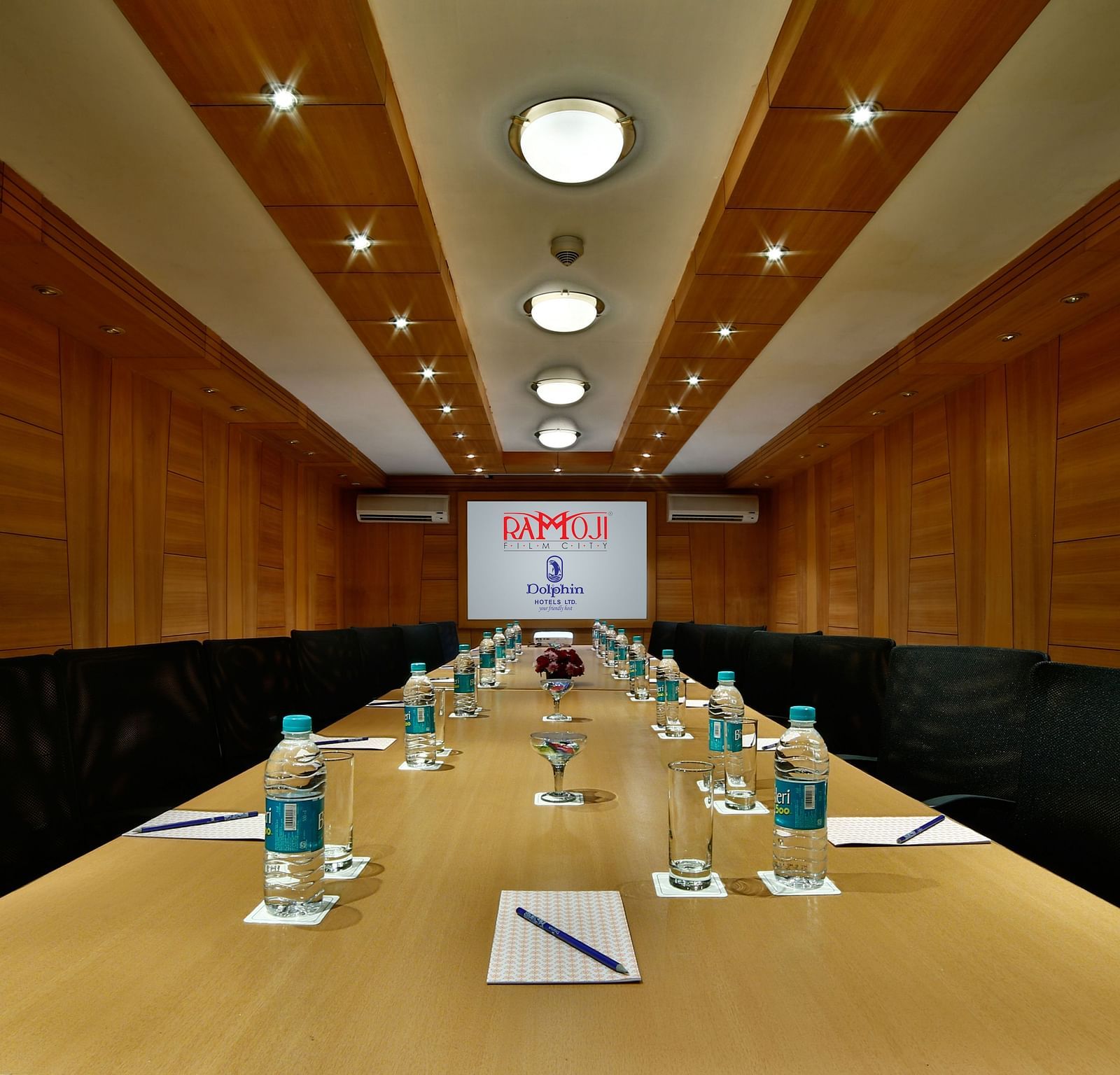 A sleek boardroom with a wooden table, leather chairs, and a screen for presentations. - Tara, Comfort Hotel in Hyderabad - Ramoji Film City.