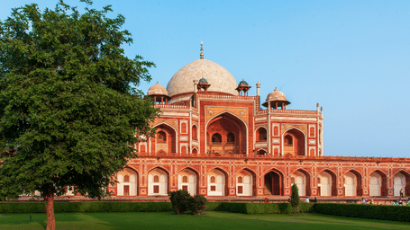 Exterior view of a historical dome monument featuring traditional stone architecture, manicured lawn area, surrounding trees in the foreground.
