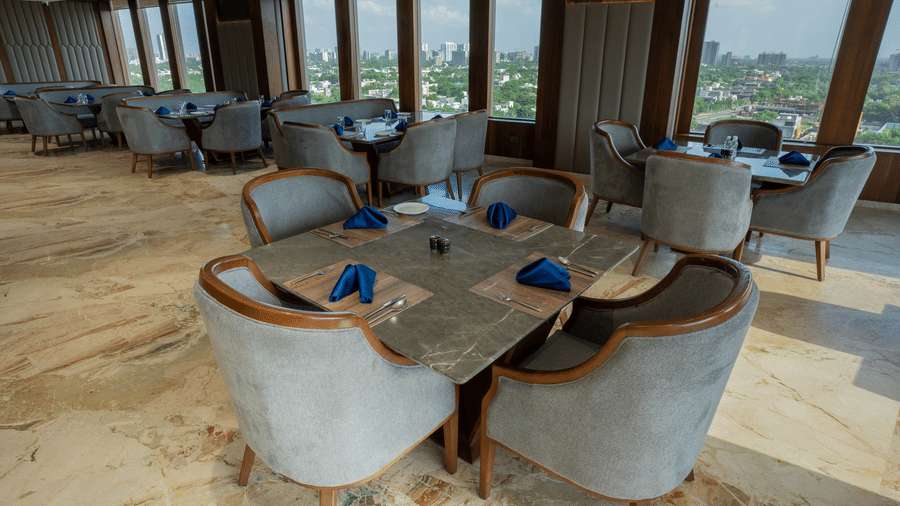 A sophisticated restaurant dining area with square stone tables and blue napkins overlooking city views - Praveg's Grand Eulogia, Ahmedabad