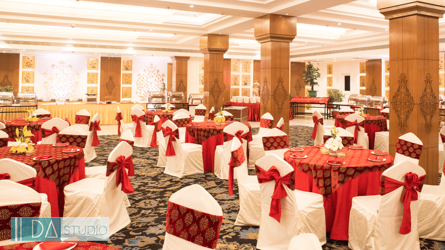 A grand banquet hall with high ceilings, large pillars, and elegant red and gold decor, with a lavish dining setup for a wedding or event - Clarks Avadh, Lucknow