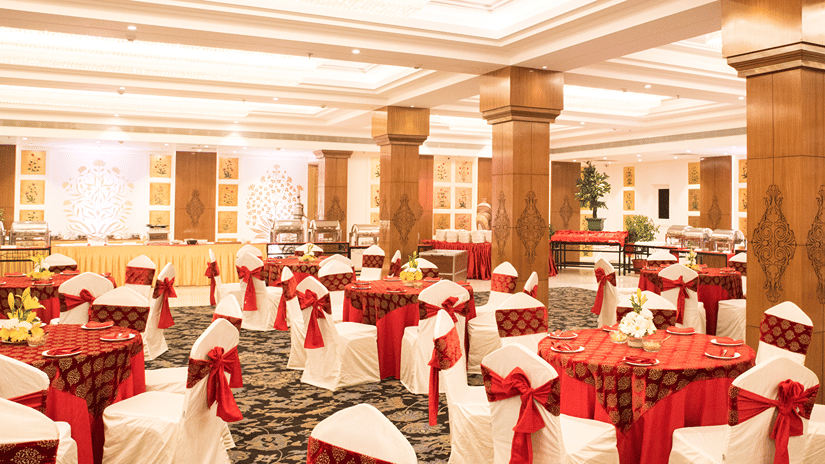 A grand banquet hall with high ceilings, large pillars, and elegant red and gold decor, with a lavish dining setup for a wedding or event - Clarks Avadh, Lucknow
