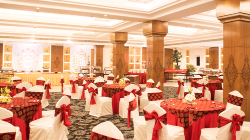 A grand banquet hall with high ceilings, large pillars, and elegant red and gold decor, with a lavish dining setup for a wedding or event - Clarks Avadh, Lucknow