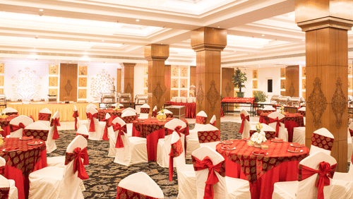 A grand banquet hall with high ceilings, large pillars, and elegant red and gold decor, with a lavish dining setup for a wedding or event - Clarks Avadh, Lucknow