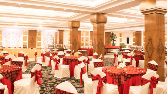 A grand banquet hall with high ceilings, large pillars, and elegant red and gold decor, with a lavish dining setup for a wedding or event - Clarks Avadh, Lucknow