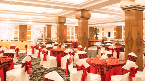 A grand banquet hall with high ceilings, large pillars, and elegant red and gold decor, with a lavish dining setup for a wedding or event - Clarks Avadh, Lucknow