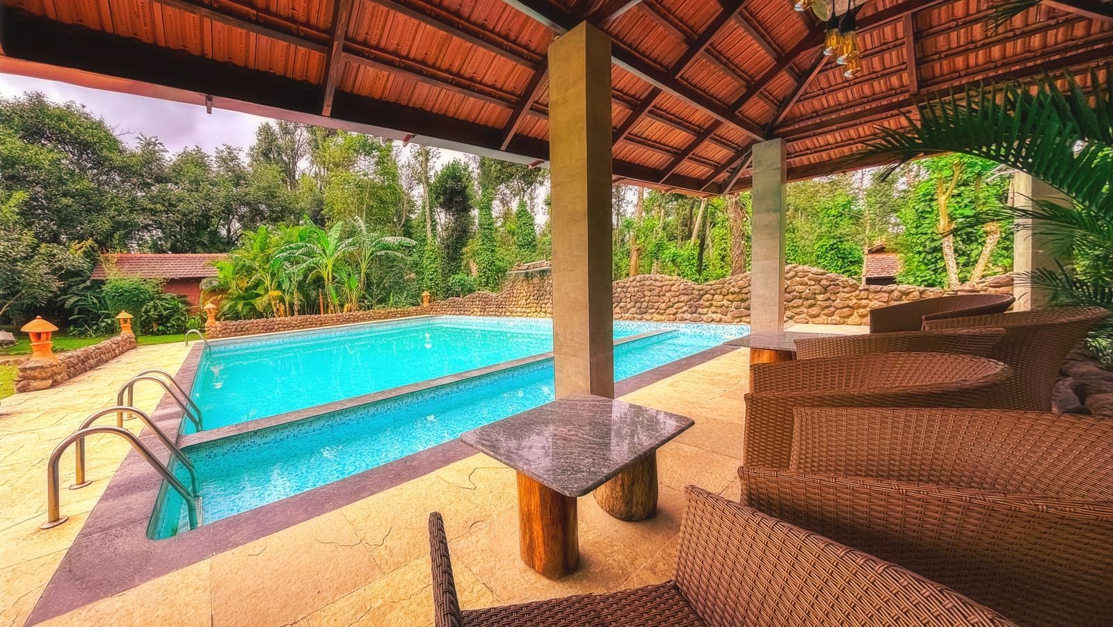 A shot of the swimming pool area at The Copper Edge - Eco Resort, Coorg, with lounge chairs and a covered seating area.