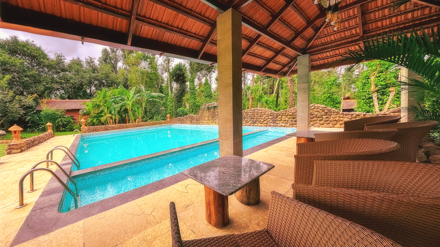 A shot of the swimming pool area at The Copper Edge - Eco Resort, one of the best resorts in Coorg with swimming pool, with lounge chairs and a covered seating area