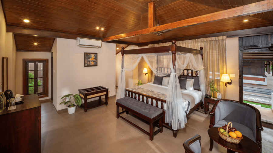 Garden View Heritage Room at Uday Backwater Resort featuring a king size four-poster bed, traditional wooden interiors, comfortable seating, and warm ambient lighting.
