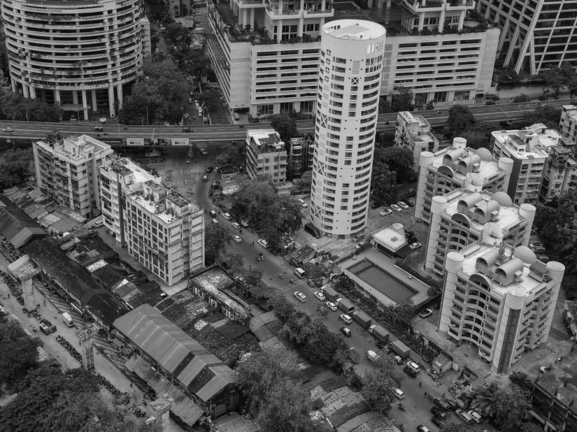 An industrial estate with it tall buildings and other warehouses in black and white. There are roads running in front and behind the tall buildings while the estate is surrounded by trees.