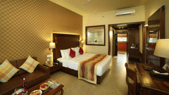 The Ocean View Room at Uday Samudra Leisure Beach Hotel & Spa, Kovalam,  features a king-size bed with decorative pillows and a patterned bed runner, a brown sofa with cushions, a wooden desk and chair and food placed on the coffee table behind.