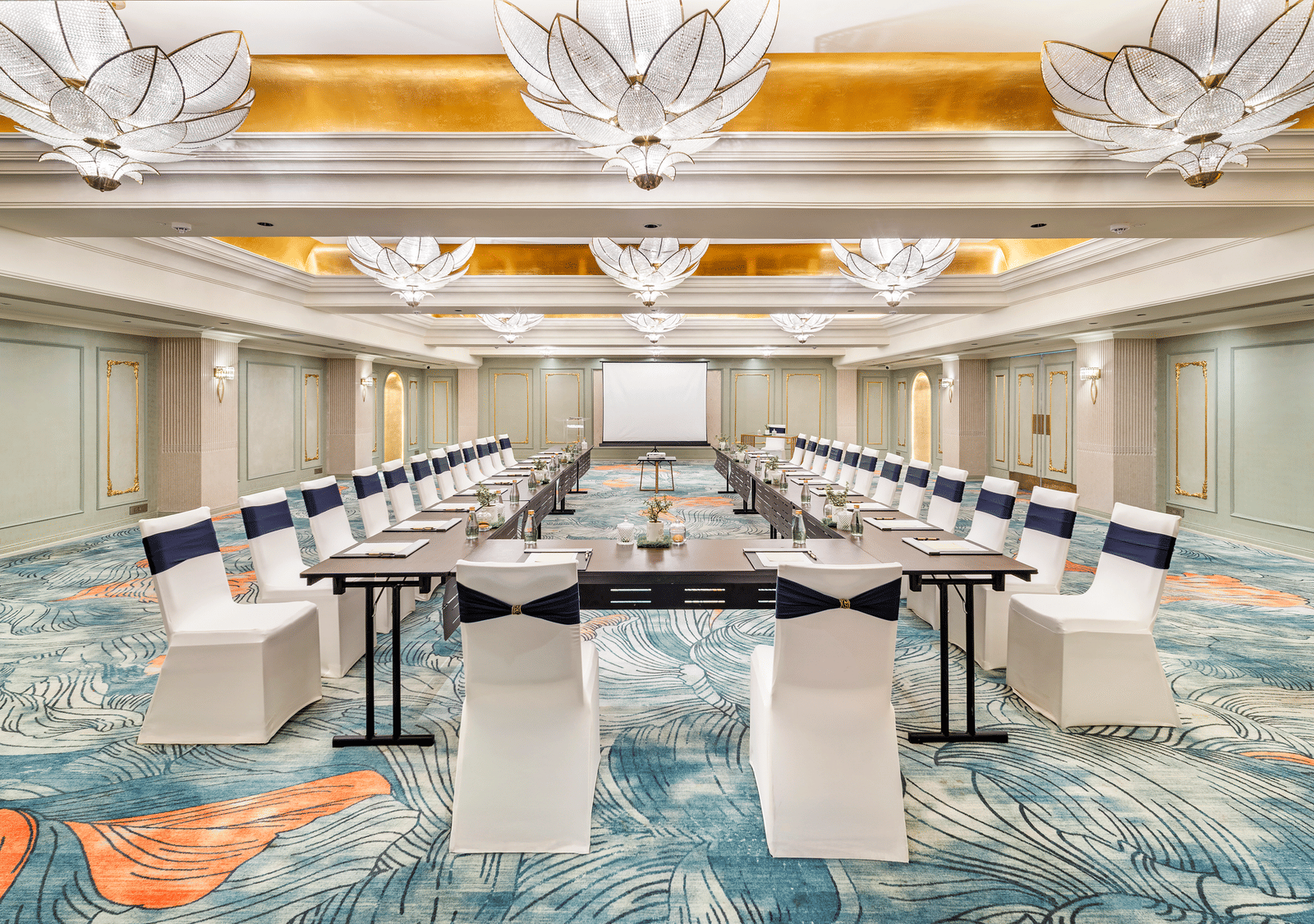 A conference or banquet hall by Grand Chennai at GRT Hotels, featuring a U-shaped arrangement of draped tables and white chairs, ready to host an important meeting or an elegant seated event.
