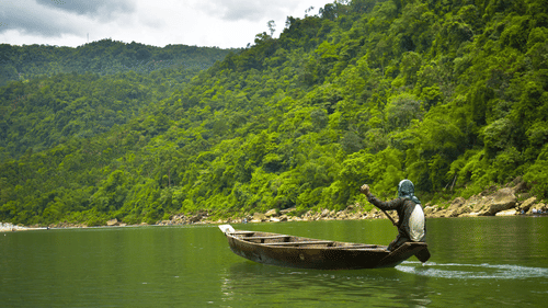 a man boating along the lush green mountains of Meghalaya