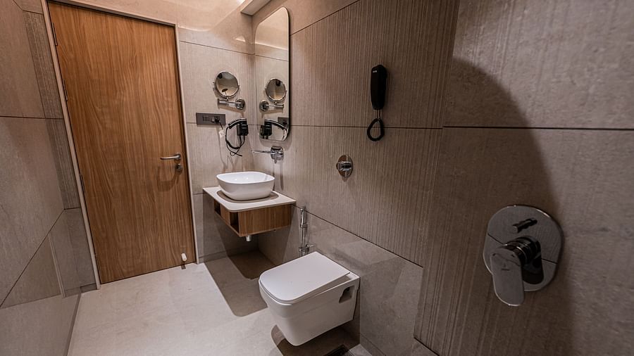 A spacious washroom at Indie Stays Mumbai International Airport, complete with a wooden door, a wall-mounted mirror above the basin, a western toilet, and a shower area.