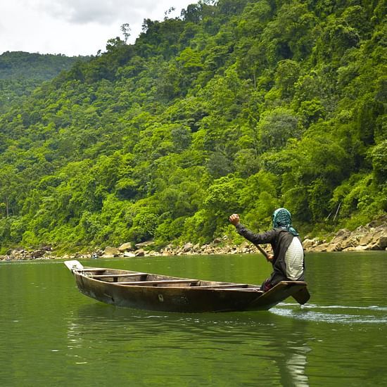 a man boating along the lush green mountains of Meghalaya