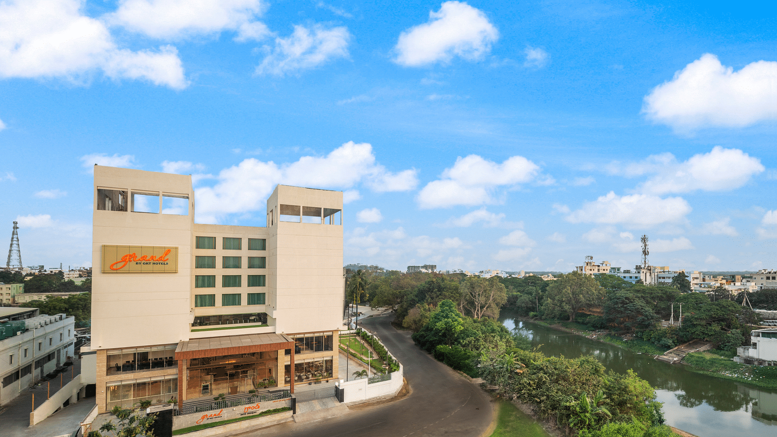 Facade image of Grand Vijayawada by GRT Hotels surrounded by folaige under a blue sky.