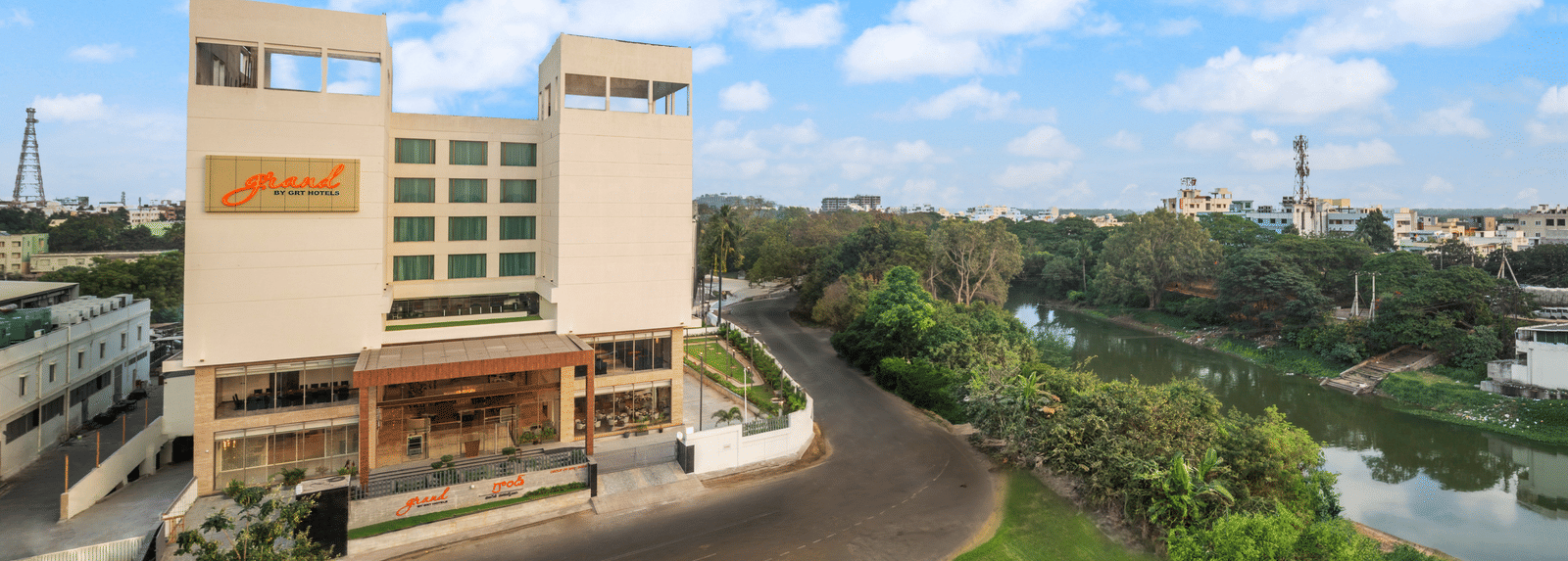 Facade of one of the best hotels in Vijayawada near Durga Temple, Grand Vijayawada by GRT Hotels surrounded by foliage under a blue sky.