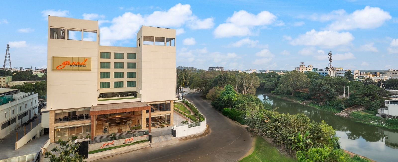 Facade of one of the best hotels in Vijayawada near Durga Temple, Grand Vijayawada by GRT Hotels surrounded by foliage under a blue sky.