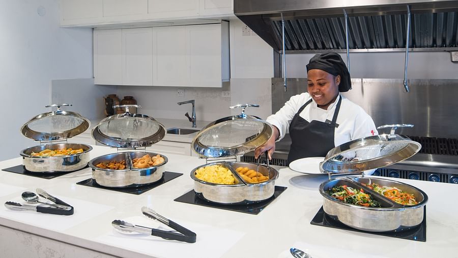 A woman with a hairnet and apron cooking meals in a kitchen - S Hotel Montego Bay, Jamaica